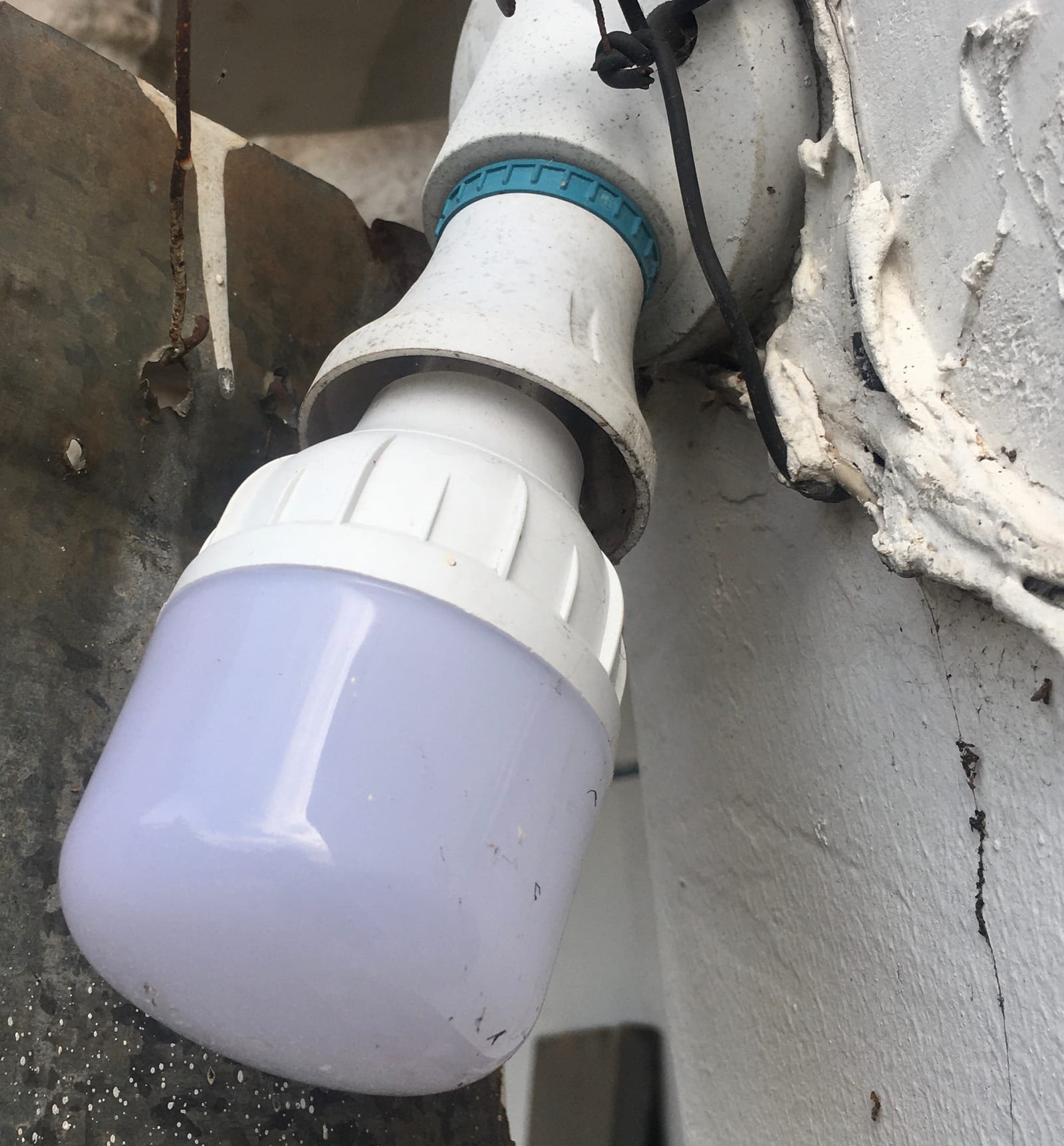 White LED bulb screwed into a plastic bulb holder next to an outside wall