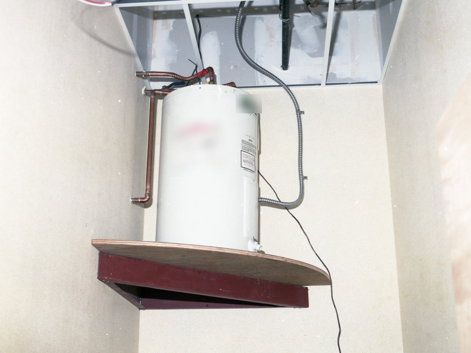 An electric tank water heater on a wooden shelf in a corner