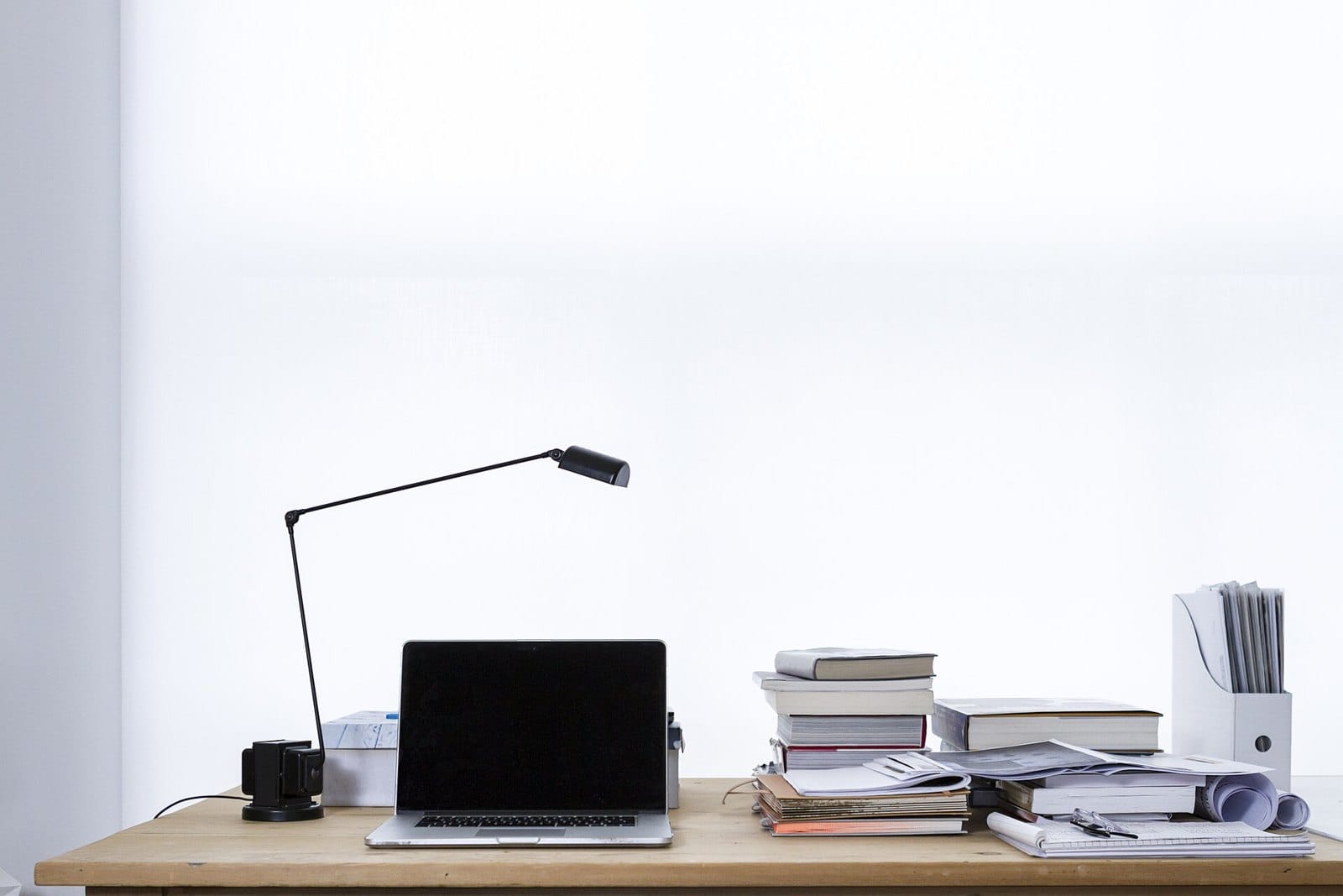 Una computadora portátil sobre una mesa de trabajo, con una lámpara y libros