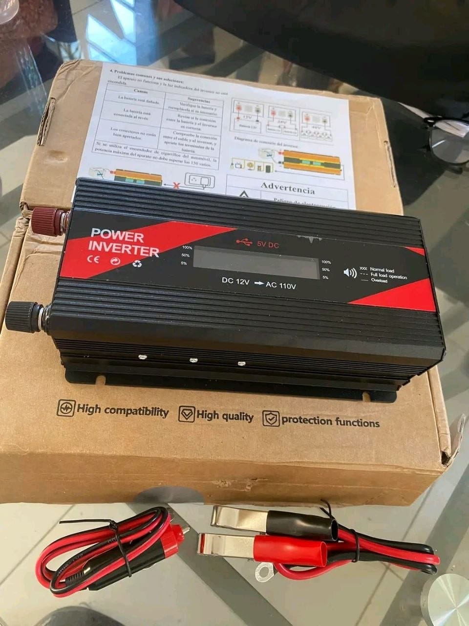 A black and red power inverter, 12 V in and 110 V out, sitting on its box with its battery clamp cables in front