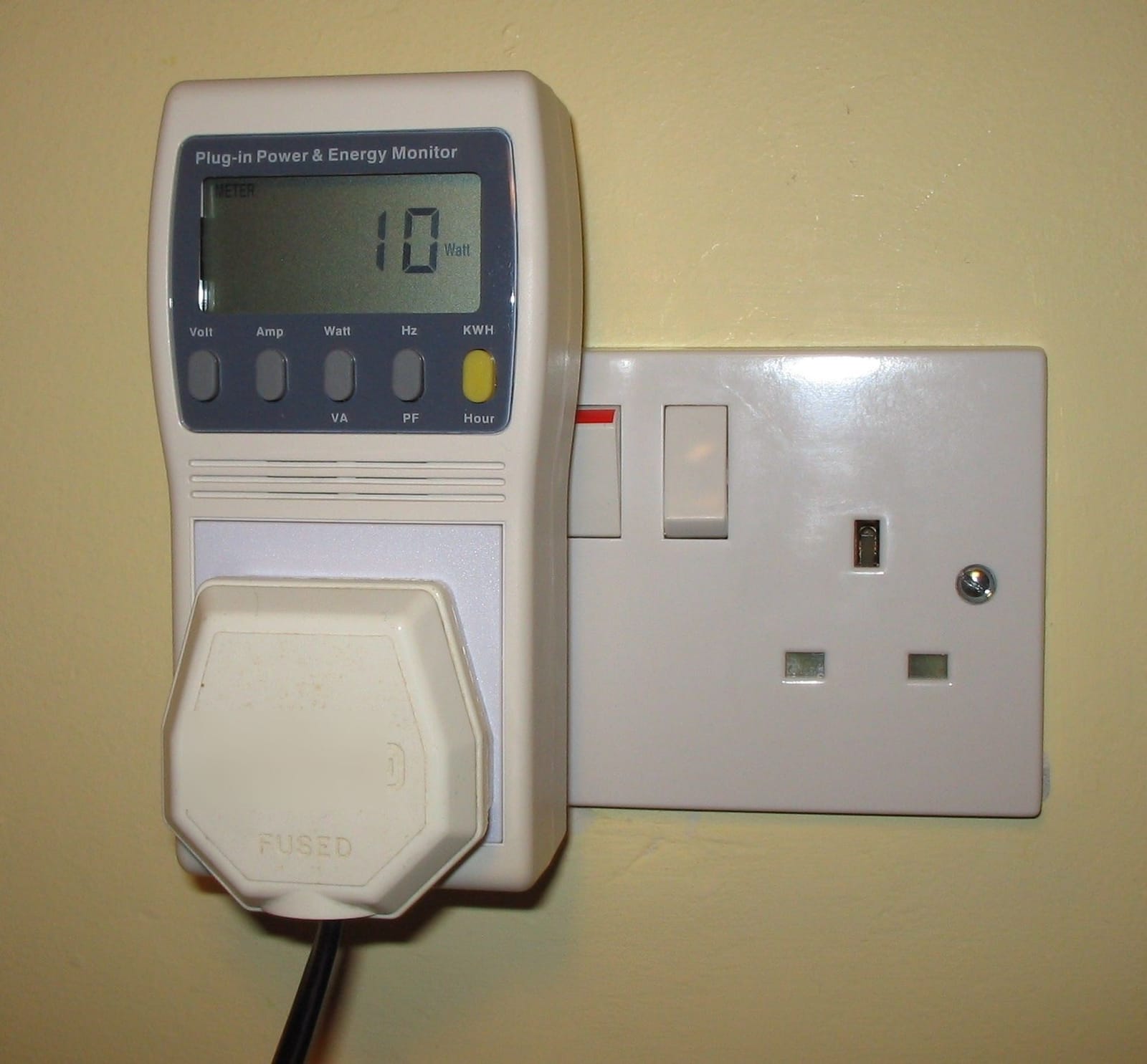 Plug-in energy monitor plugged into a wall socket, its display showing the watts used by the connected appliance