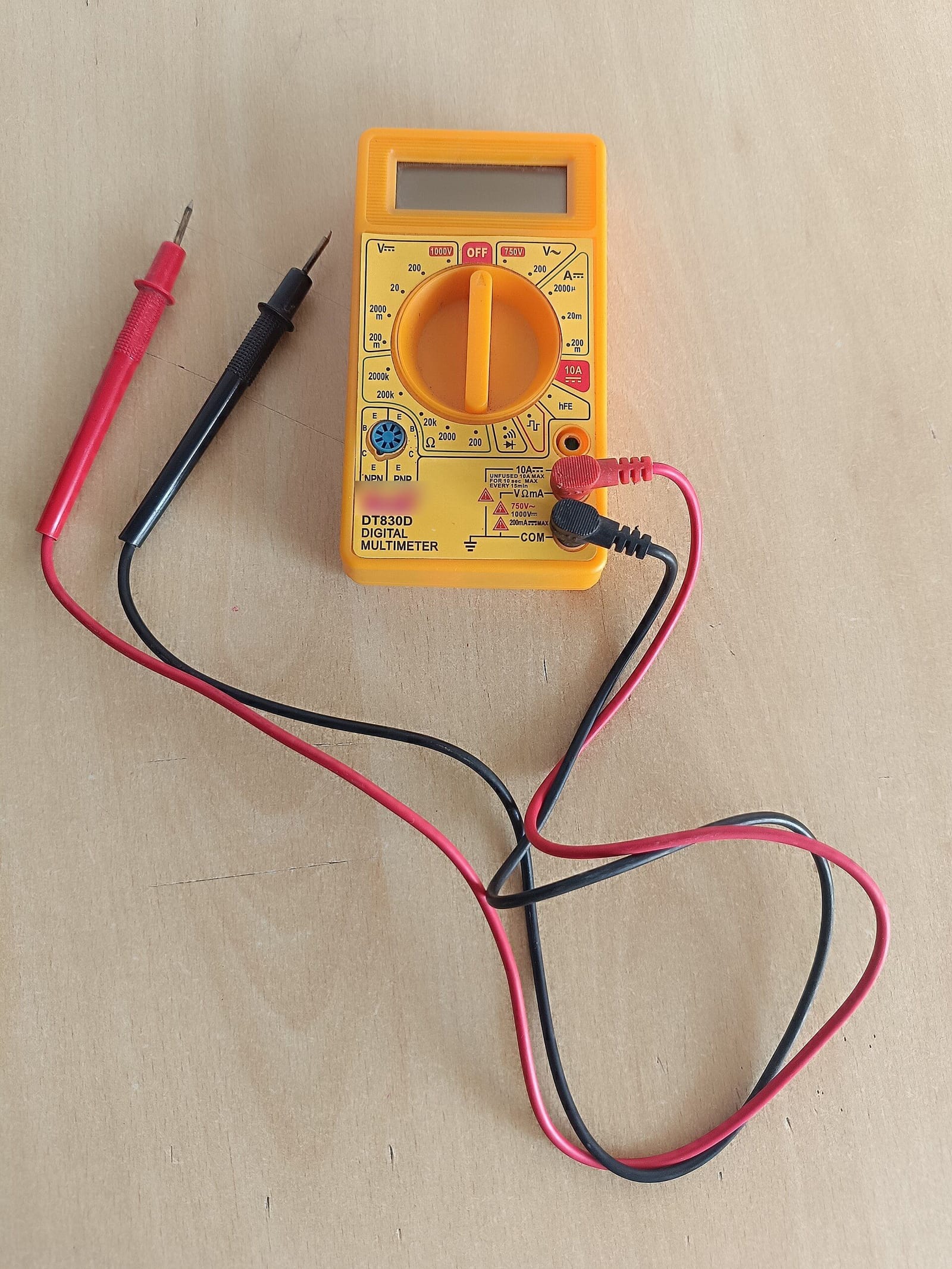 Multímetro digital amarillo con sus dos cables de medir, uno rojo y uno negro, sobre una mesa de madera
