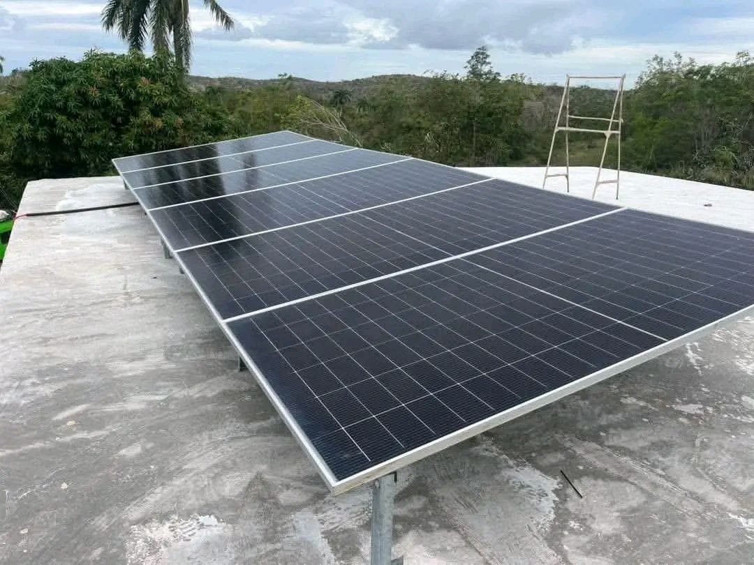 Solar panels on a metal frame on a flat house roof, with trees and hills in the background