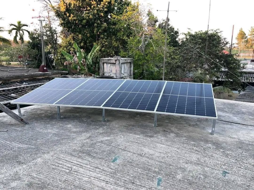Eight tilted solar panels on a frame with metal legs on a concrete flat roof, with trees behind