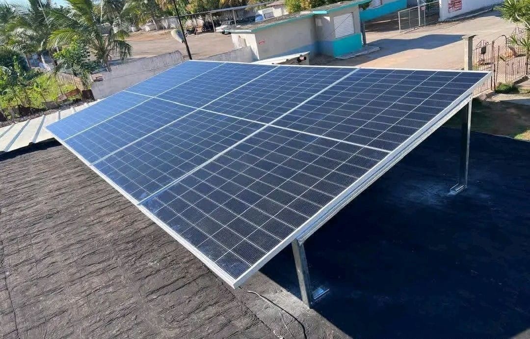 Solar panels on a tall metal frame above a house roof, with palm trees in the background