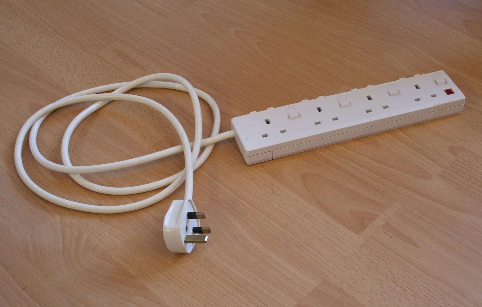 White four-socket power strip with a separate switch for each socket, its cable coiled on a wooden floor